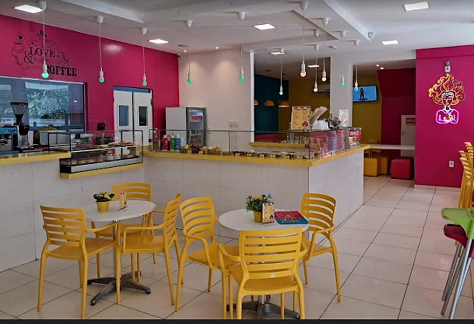 Salão da Me Gusta com paredes rosa, cadeiras amarelas, balcão de doces e o neon da mascote